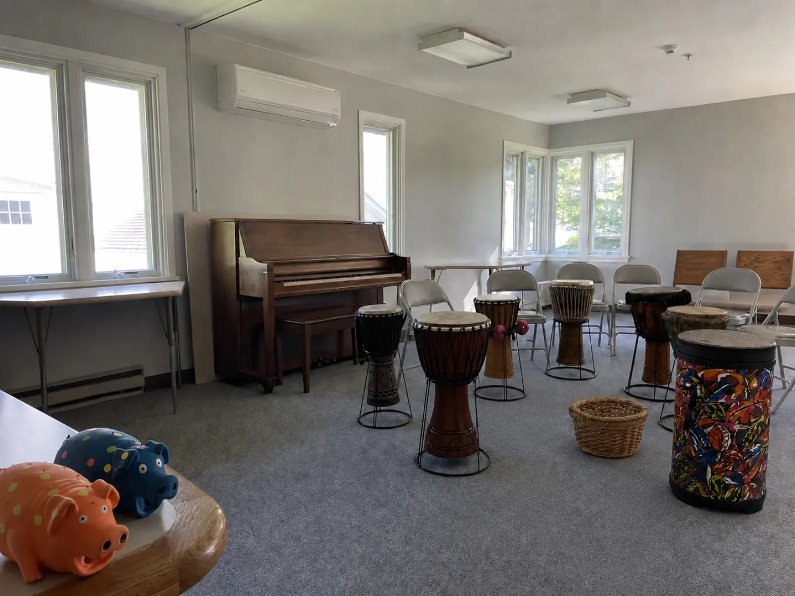 Bright meeting room set up with chairs and a circle of drums, with two pig mascots in the foreground